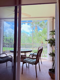 Step onto your private screened balcony, where comfortable seating invites you to relax and soak in lush tropical garden views beneath bright blue skies.