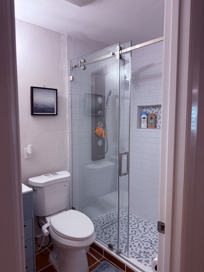 Step into your pristine, modern bathroom with a sleek glass shower, bright white tile, and all the essentials for a refreshing start to your day.