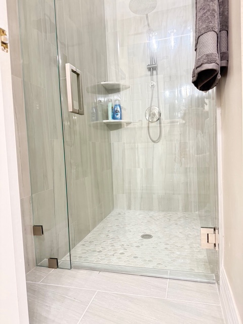 Step into your sleek glass-enclosed shower with rainfall head and built-in shelving for ultimate relaxation.
