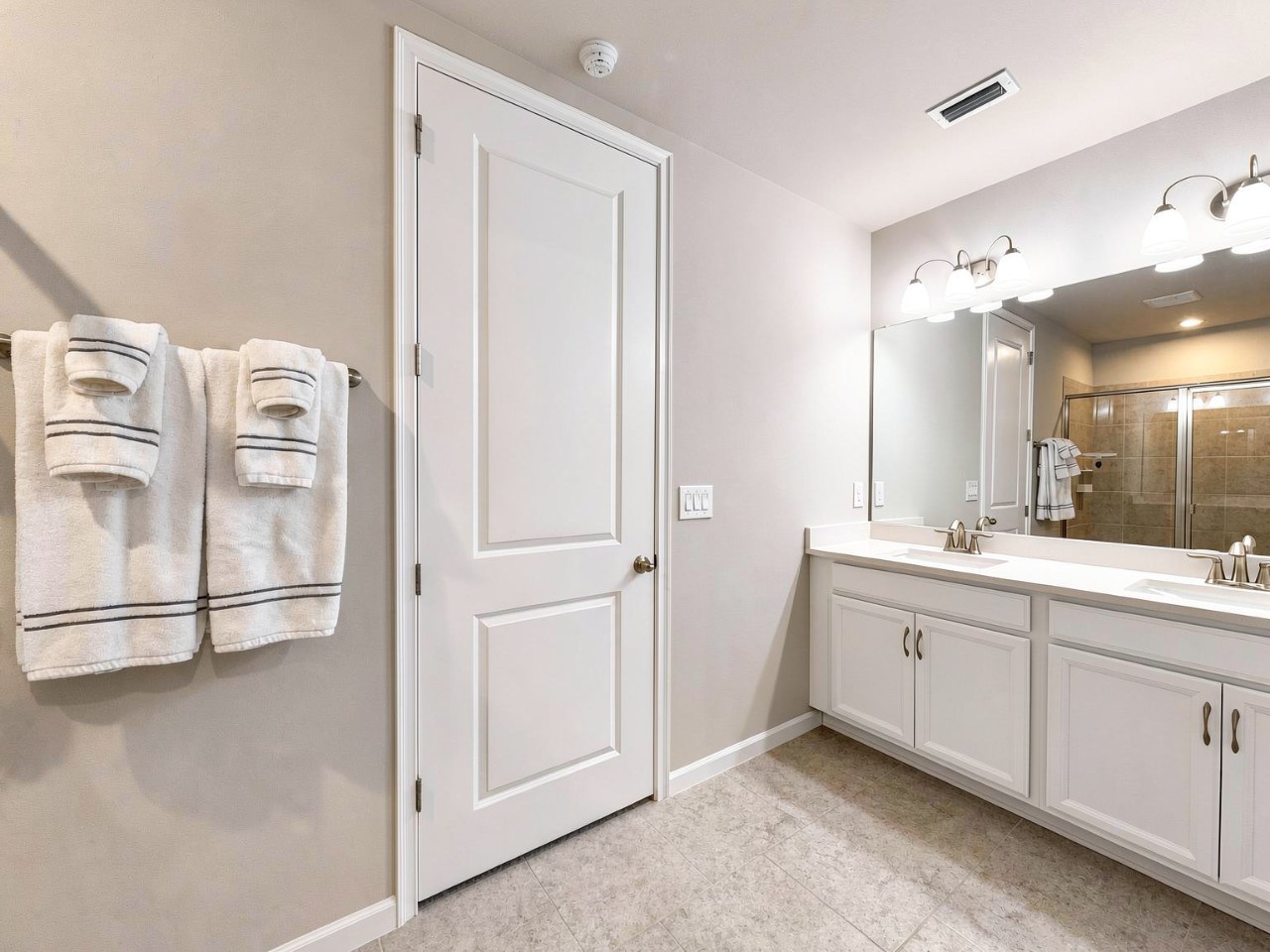 Step into your crisp, modern bathroom with fresh white cabinetry, warm vanity lighting, and plush towels waiting to welcome you after a refreshing shower.