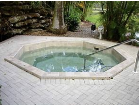 Soak your cares away in your private hexagonal hot tub, nestled among lush gardens and natural stone—your perfect outdoor retreat after a day exploring.