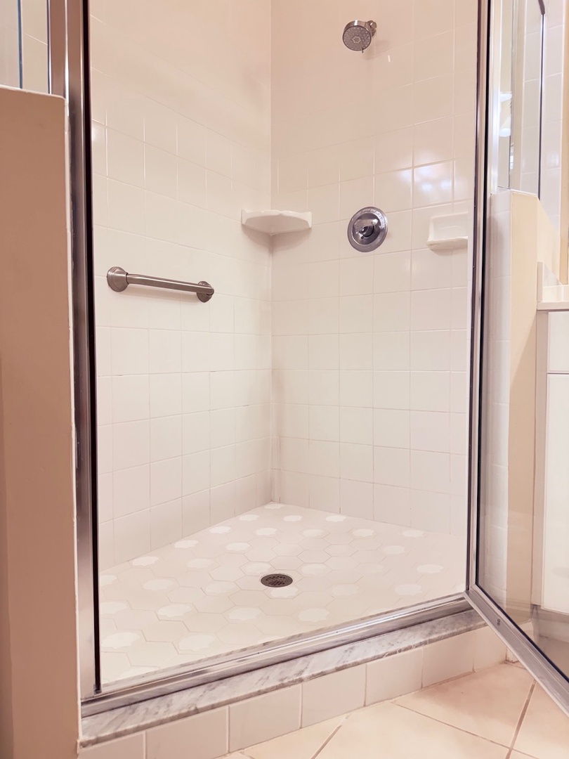 Step into your private walk-in shower with sleek white tile, a rainfall showerhead, and grab bar for safety. The glass enclosure keeps things bright and open—perfect for refreshing mornings.