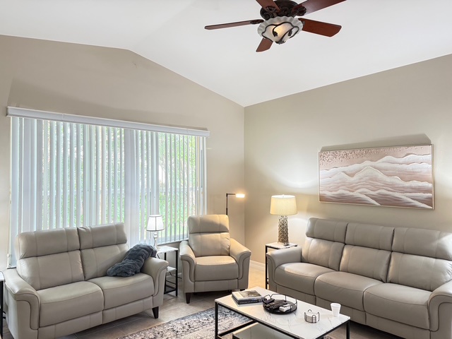 Unwind in your spacious living room with plush gray seating, warm lighting, and a gentle ceiling fan creating the perfect atmosphere for relaxation.