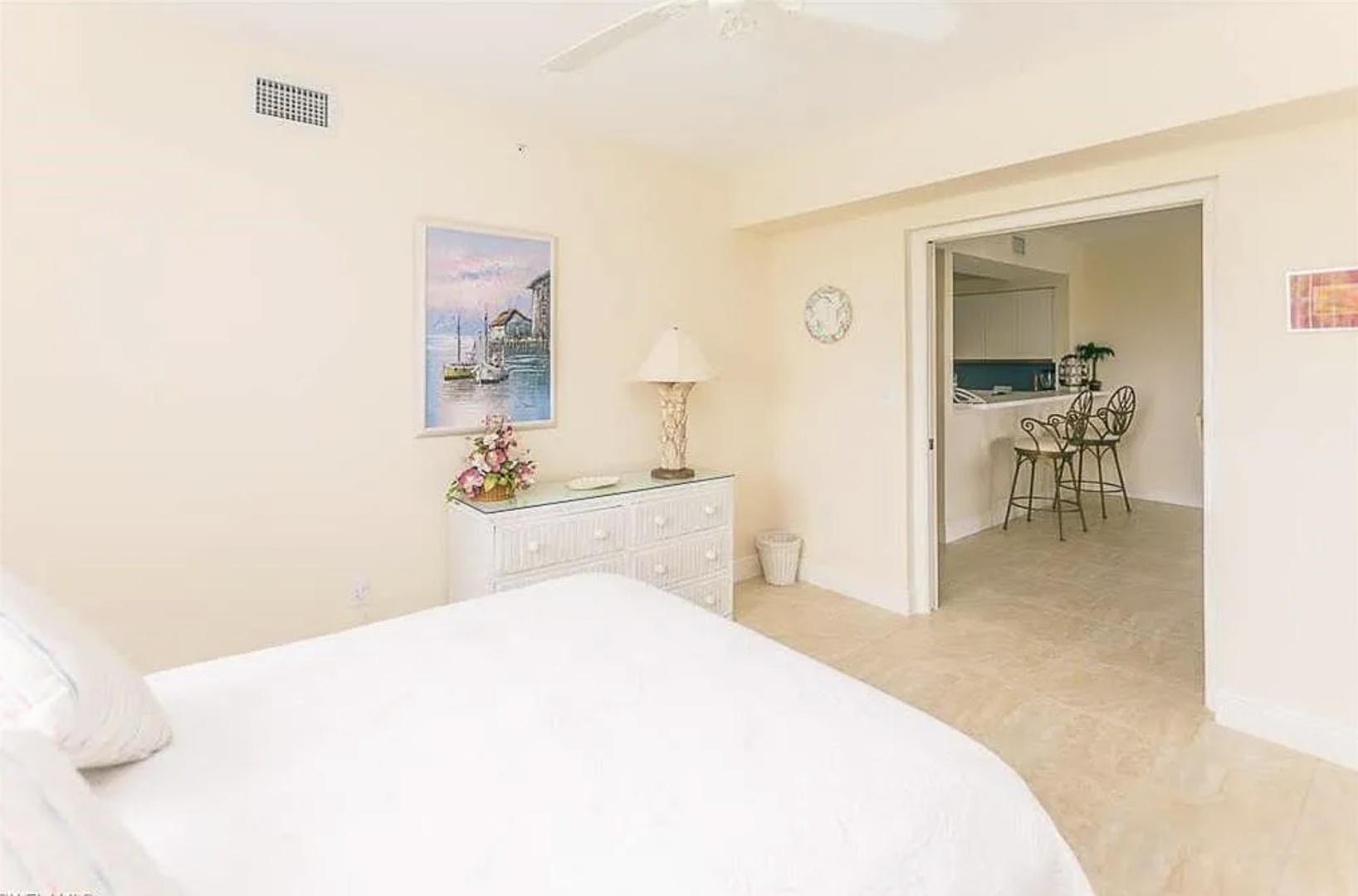 Step into your serene bedroom, where soft white linens and vaulted ceilings create an airy retreat. A charming dining area awaits just beyond, making mornings here feel effortless and bright.