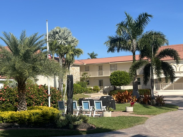 The property features tropical landscaping with palm trees and colorful flowering plants set against a clear blue sky.