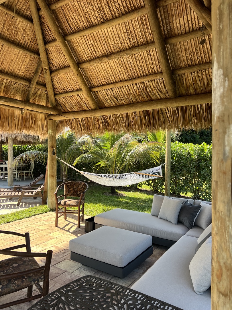 Relax under natural thatched roofing while enjoying your private hammock overlooking tropical gardens and modern outdoor seating.