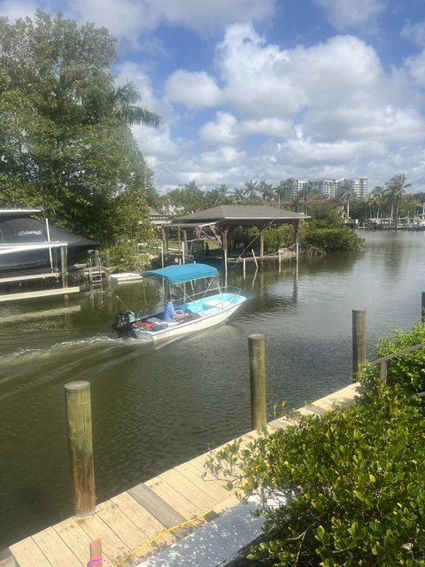 Your private dock awaits on a peaceful canal, offering direct waterfront access for boat excursions. Lush greenery and covered boat slips frame the view across calm waters under a Florida sky.