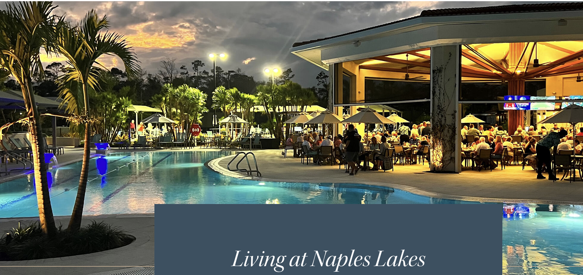 An outdoor pool with curved edges and illuminated features sits beside an open-air dining area as the evening sky transitions overhead.