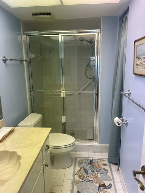Your private bathroom features a spacious walk-in shower with sleek glass doors, a peaceful blue color palette, and coastal décor that sets a relaxing tone for your stay.