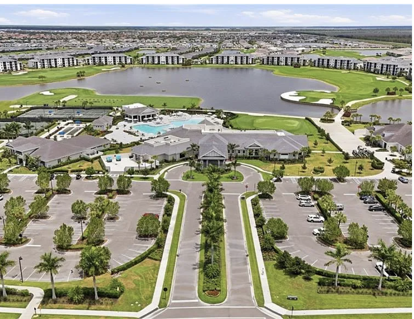 An aerial view captures the resort-style community featuring manicured lawns, a large lake, golf course greens, swimming pool, and well-planned grounds surrounded by residential buildings.