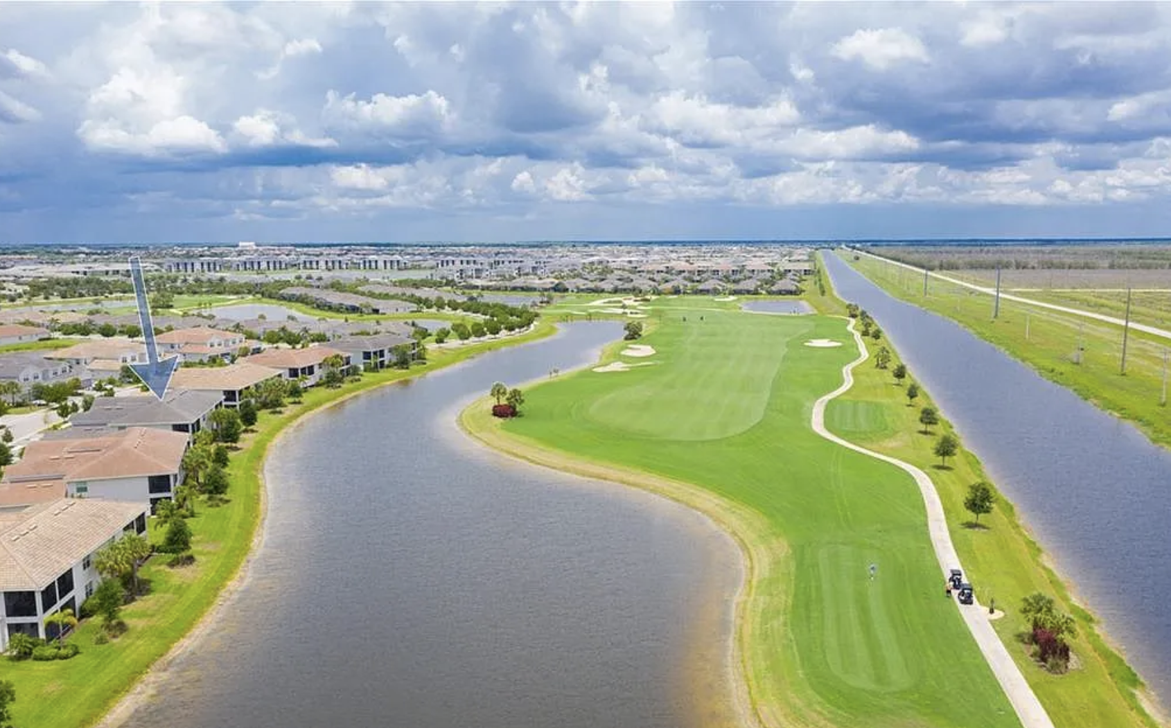 Aerial view showcasing the championship golf course winding through the resort community, flanked by scenic waterways and distant residential buildings under expansive Florida skies.