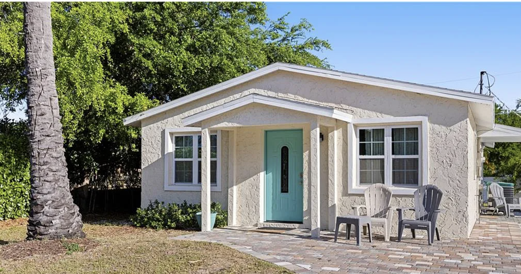 A charming beachside cottage with a welcoming turquoise door and shaded front porch awaits your coastal getaway.