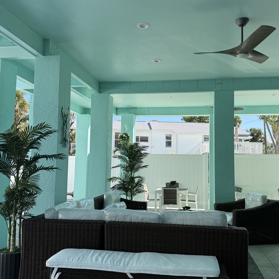 Unwind in this breezy covered terrace where tropical palms and plush seating create your perfect coastal retreat.