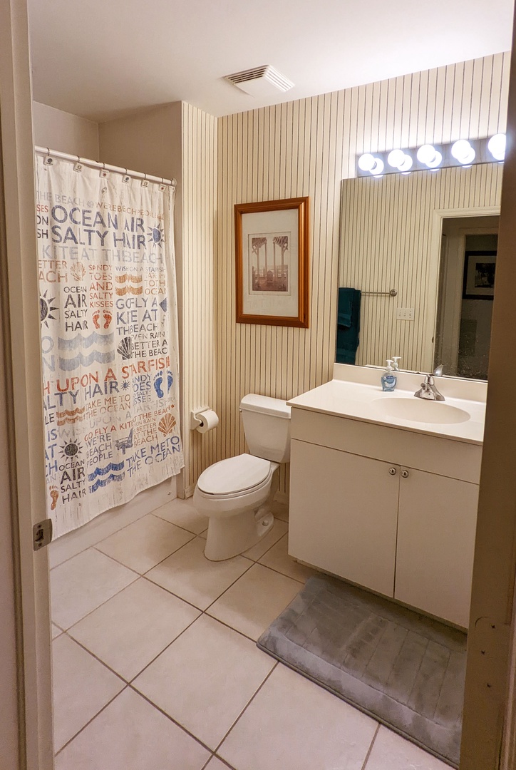 Your coastal-themed bathroom features a bright vanity with Hollywood-style lighting and cheerful ocean-inspired shower curtain for refreshing morning routines.