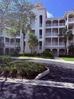 Multi-story vacation property surrounded by lush landscaping and mature trees, featuring arched balconies and Mediterranean-style architecture under sunny Florida skies.