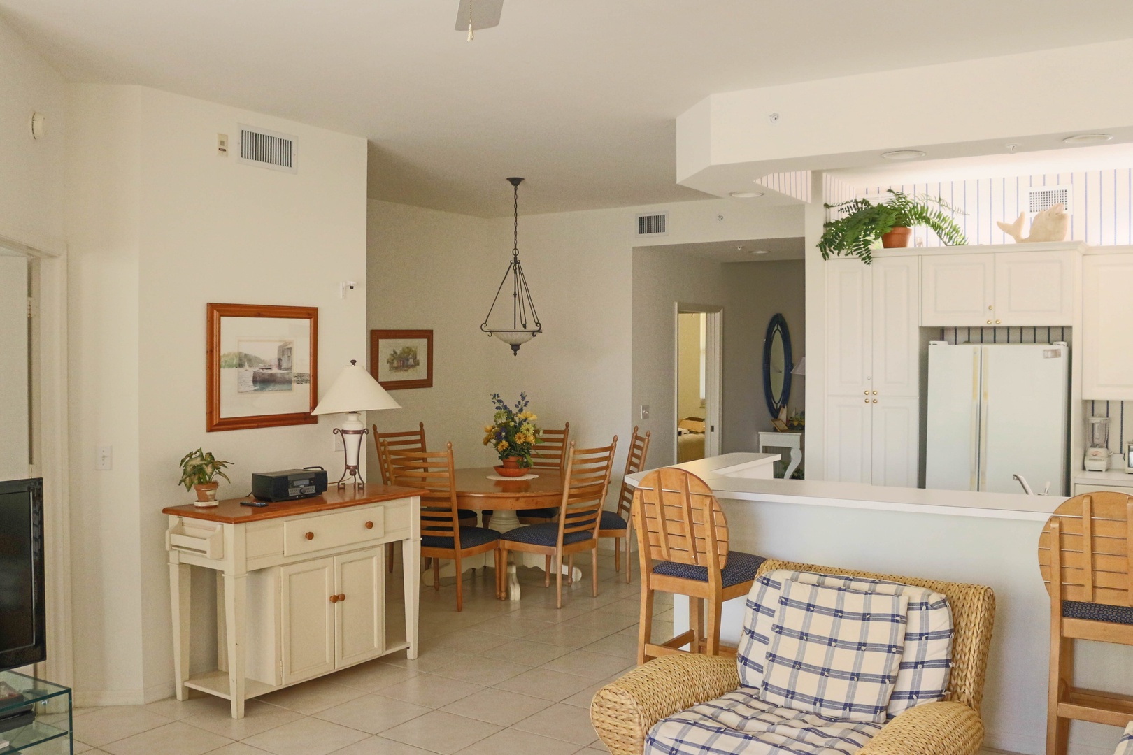 Relax in your bright, open-concept living space featuring coastal charm with wicker seating, warm wood furnishings, and seamless kitchen access.