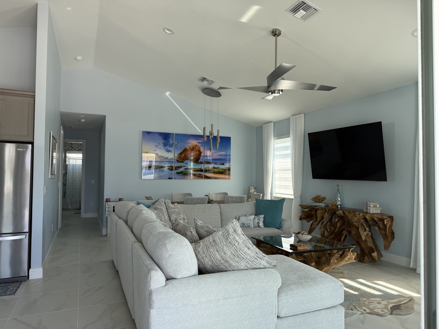 Relax in your stylish open-concept space featuring a plush sectional, coastal artwork, and natural wood accents that create the perfect beach house atmosphere.