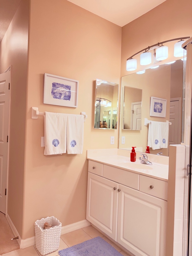 Your private bathroom features crisp white cabinetry, fresh linens with thoughtful decorative touches, and warm lighting to help you feel right at home after a day exploring.