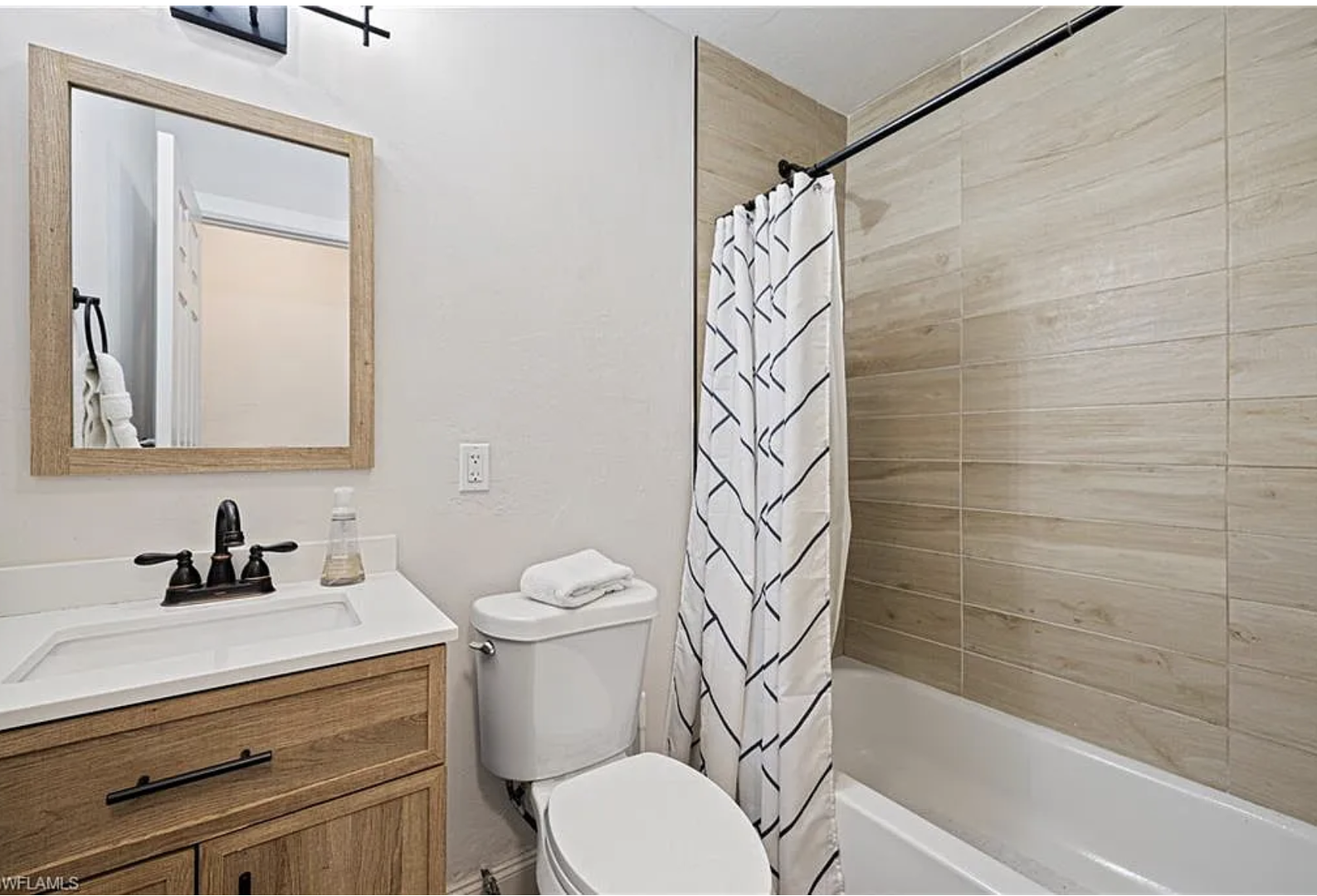 Step into a stylishly updated bathroom with warm wood-tone tiles, contemporary vanity, and fresh linens waiting for your arrival.