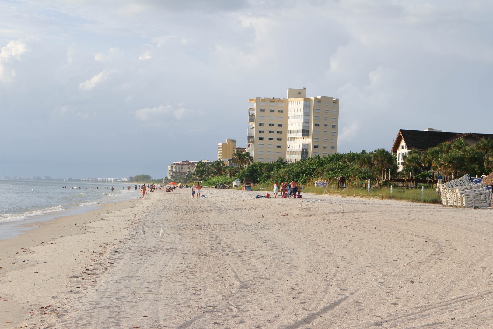 Expansive beachfront with soft sand stretches along the coastline, framed by modern buildings and lush tropical vegetation.