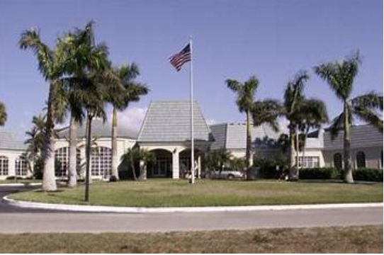 The property sits in a tropical-palm-lined neighborhood with well-maintained grounds and classic architecture featuring a distinctive roofline and central flag display.