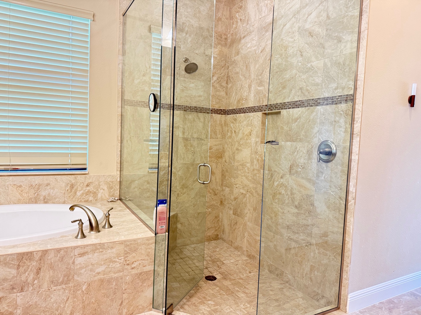 Unwind in your elegant bathroom featuring a spacious glass shower with natural stone tile and relaxing soaking tub.