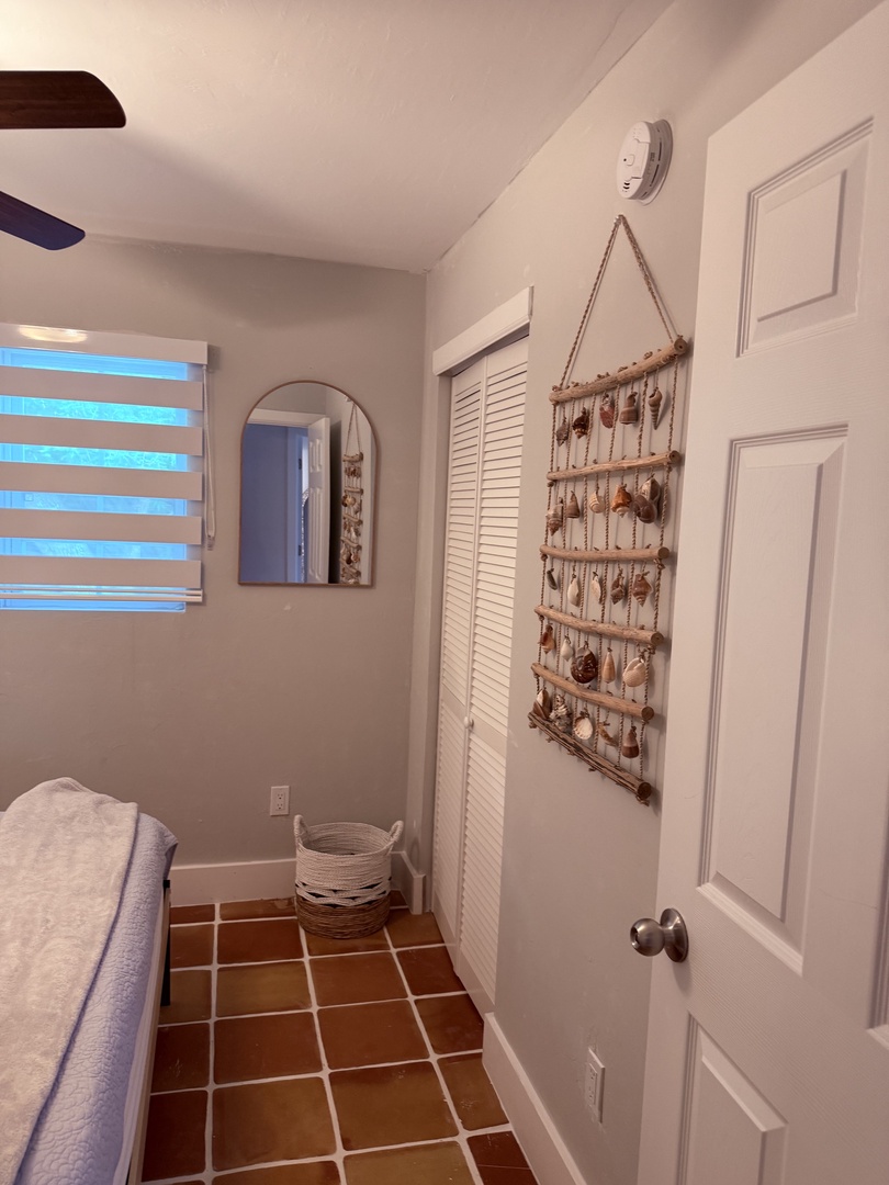 Your bedroom blends coastal charm with clever modern touches. A rustic shuttered ceiling panel adds character overhead, while warm terracotta-tiled walls create an inviting glow that welcomes you after a day exploring.