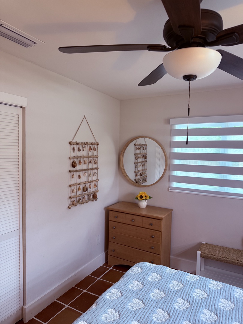 Relax in your bright, airy bedroom with a cozy quilted bed, gentle ceiling fan, and charming coastal touches. Natural light flows through the window, creating a peaceful retreat after your day's adventures.