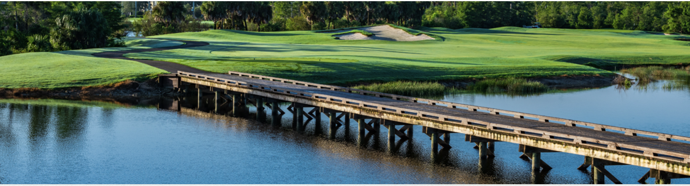 The golf course features manicured fairways, strategic sand traps, and a scenic wooden bridge crossing a tranquil water hazard—a beautiful backdrop for the property.