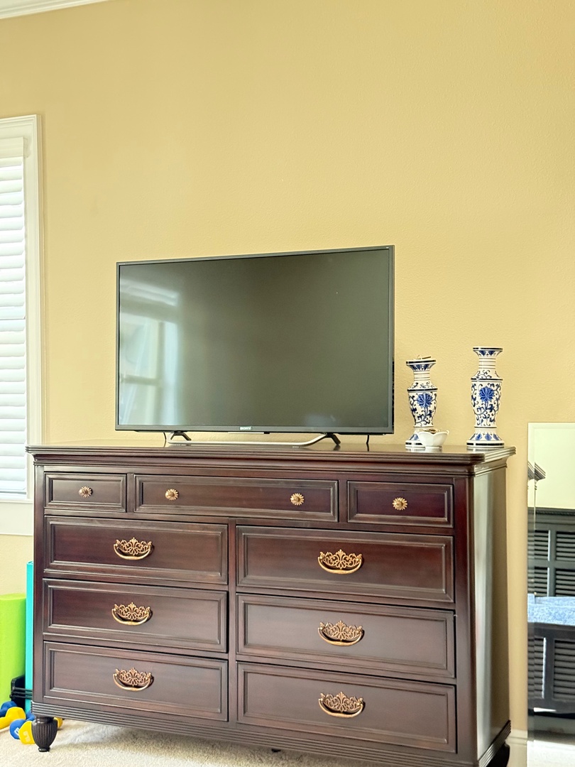 Your elegant entertainment center features a sleek flat-screen TV and beautiful wooden wardrobe with ornate handles for storing your belongings.