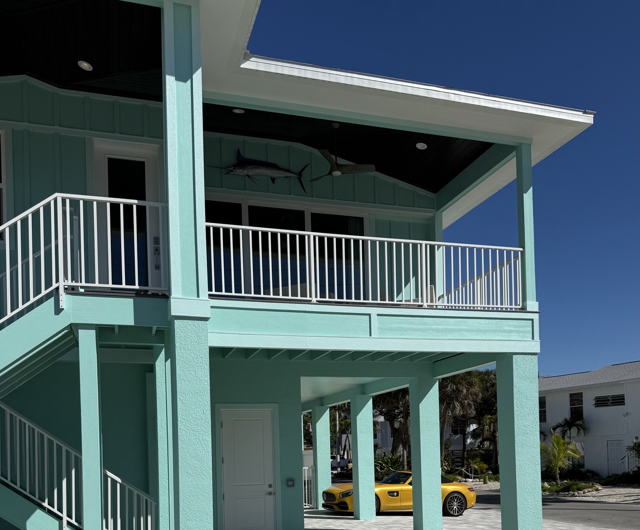 This charming turquoise beach house offers elevated living with covered parking and a spacious upper-level balcony perfect for relaxation.