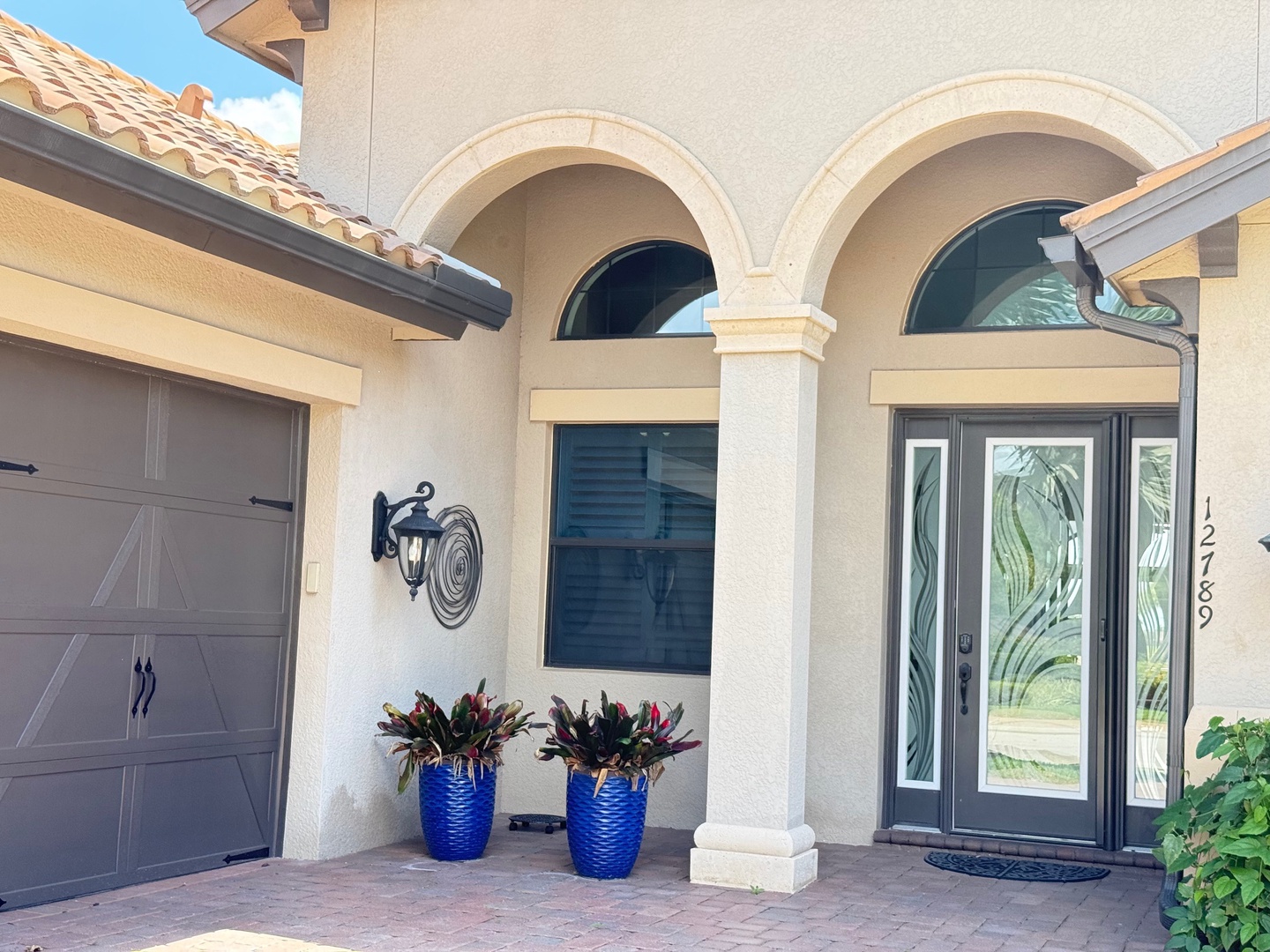 Mediterranean-style entrance features elegant arched columns, decorative lighting, and vibrant blue planters welcoming guests to this distinctive vacation rental property.