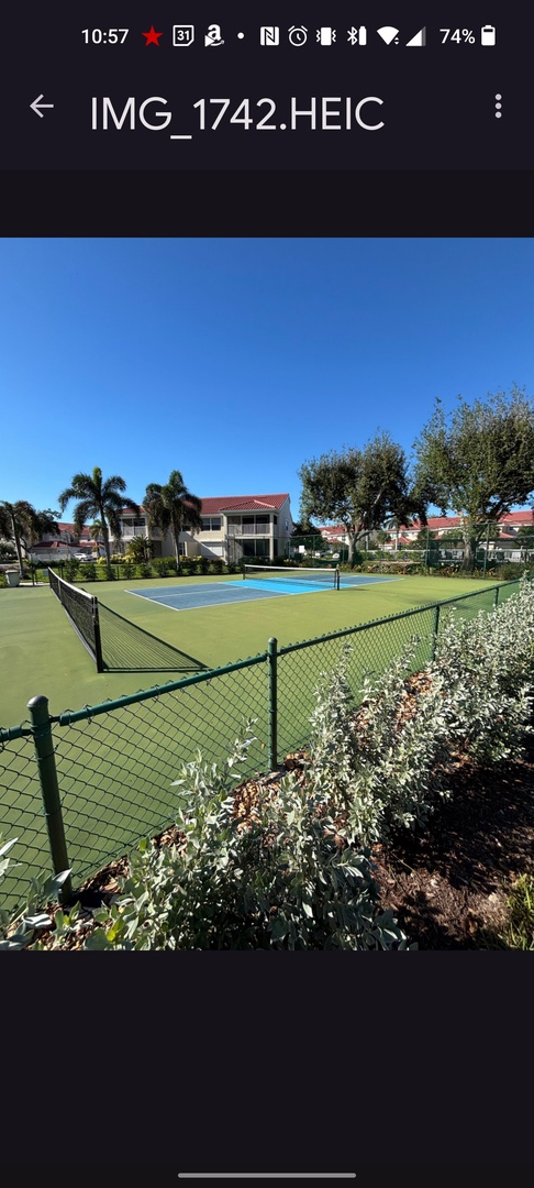 Challenge friends to a match on the private tennis court, surrounded by lush tropical landscaping and resort-style buildings.
