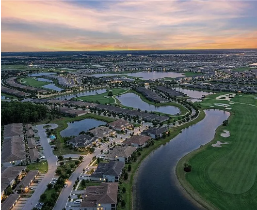 An aerial perspective captures the property's resort-style neighborhood at sunset, with winding lakes and golf fairways stretching across the landscaped community.