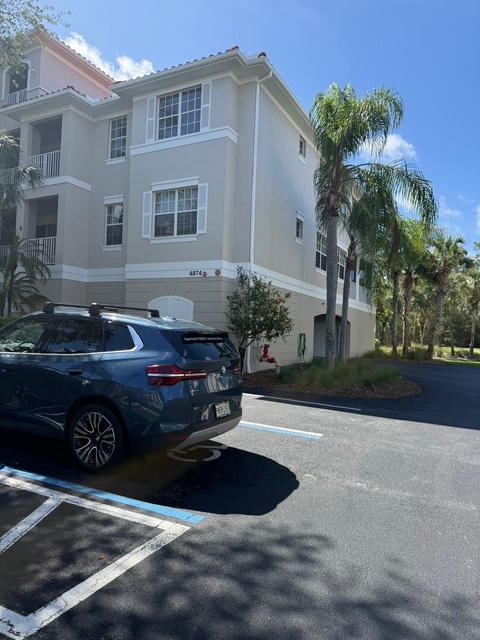 The property features a multi-story building with tropical landscaping including palm trees, surrounded by a peaceful residential setting with convenient parking.
