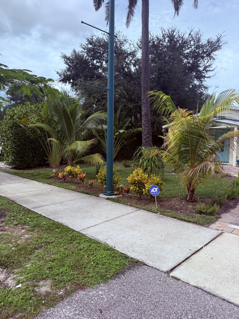 The property is located in a lush tropical neighborhood with palm trees, manicured landscaping, and convenient parking.