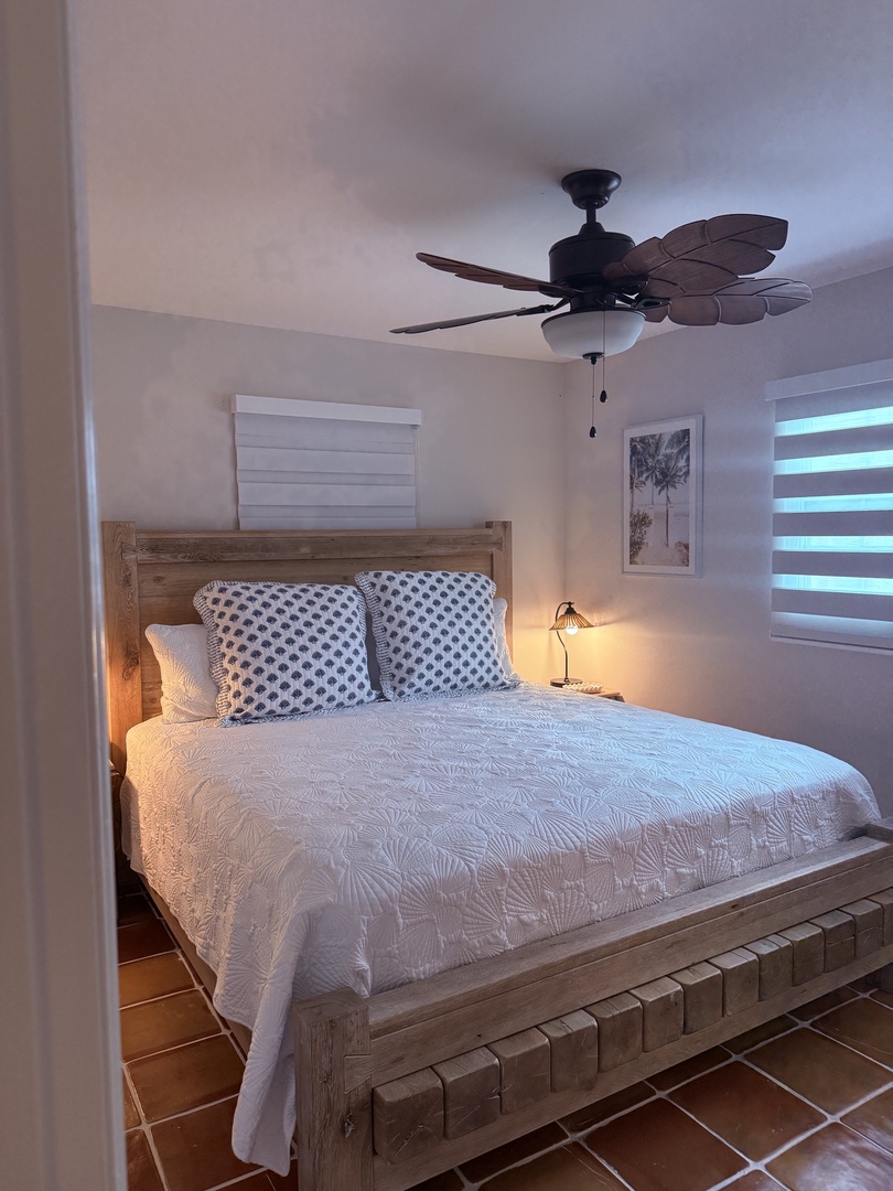 Your serene bedroom retreat awaits, with crisp white linens, warm bedside lighting, and gentle cooling from the wall fan for ultimate comfort after a day of adventure.