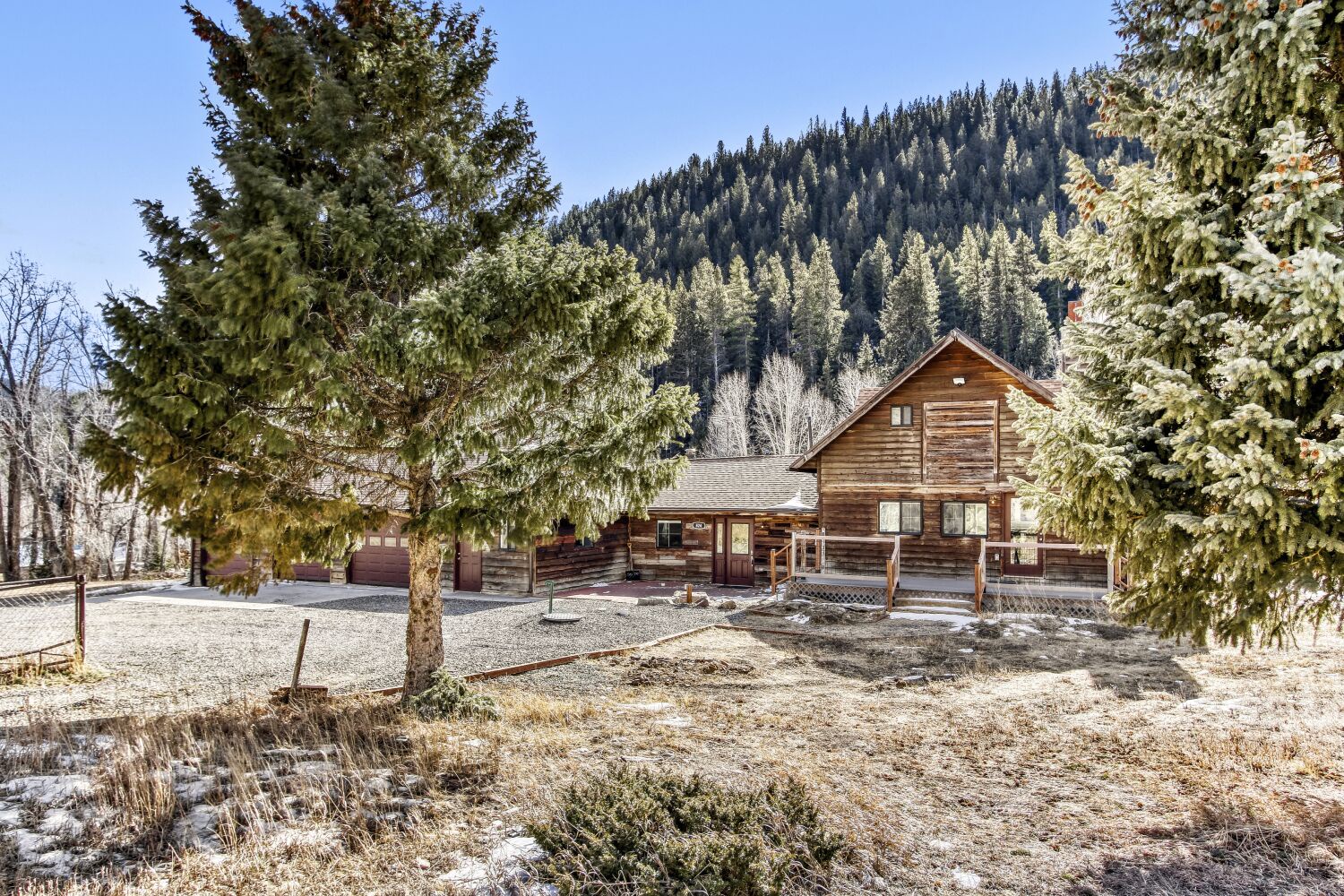 Rustic mountain cabin nestled among snow-dusted evergreens with dramatic forested peaks rising behind the peaceful property.