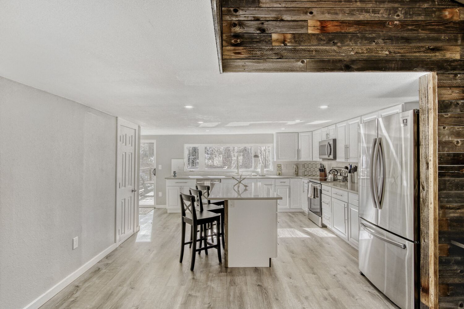 You'll love preparing meals in this spacious kitchen featuring white cabinets, stainless appliances, and a charming breakfast island with rustic wood beam details overhead.
