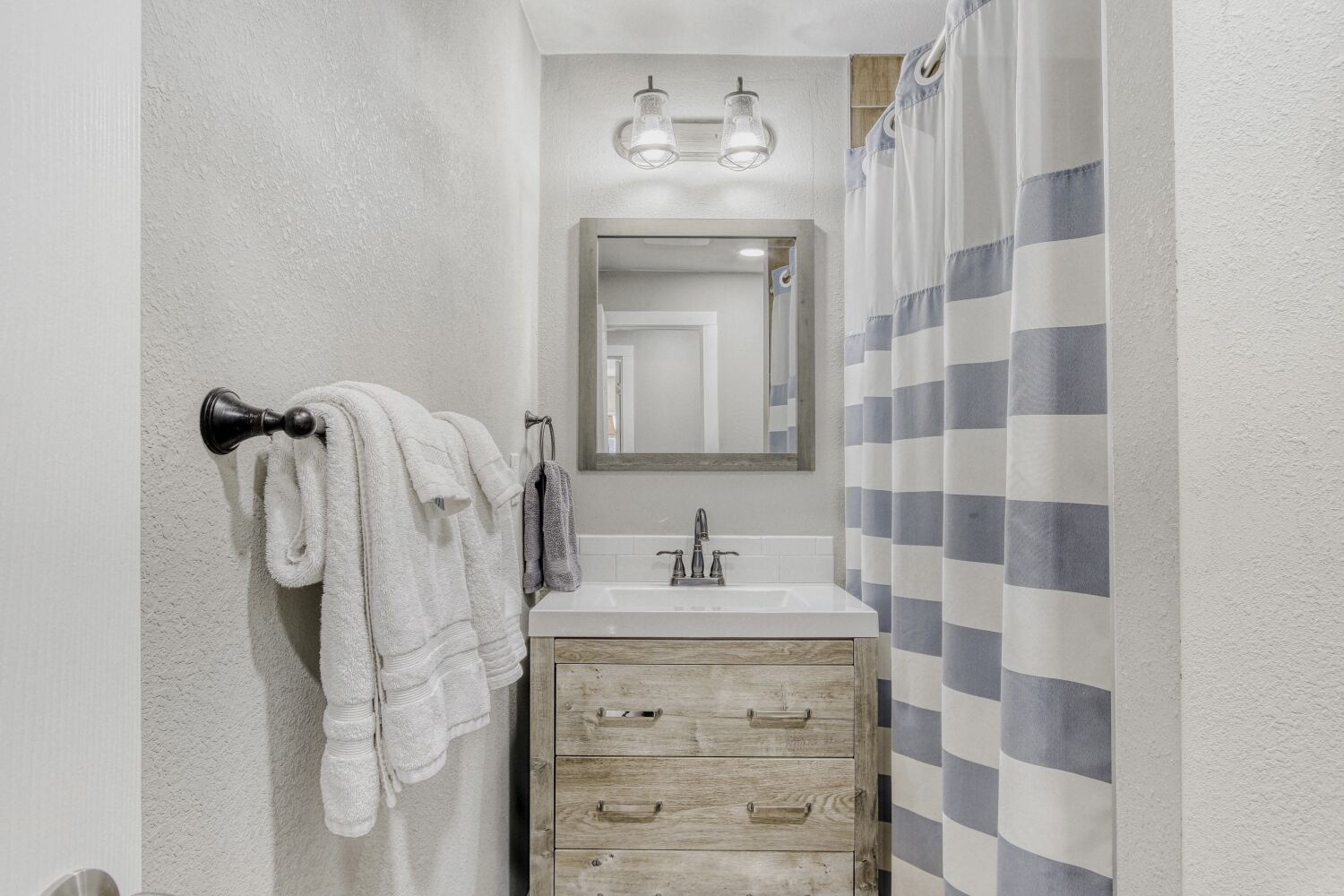Step into your bright, modern bathroom with rustic vanity, fresh towels, and charming striped shower curtain ready for your relaxing retreat.