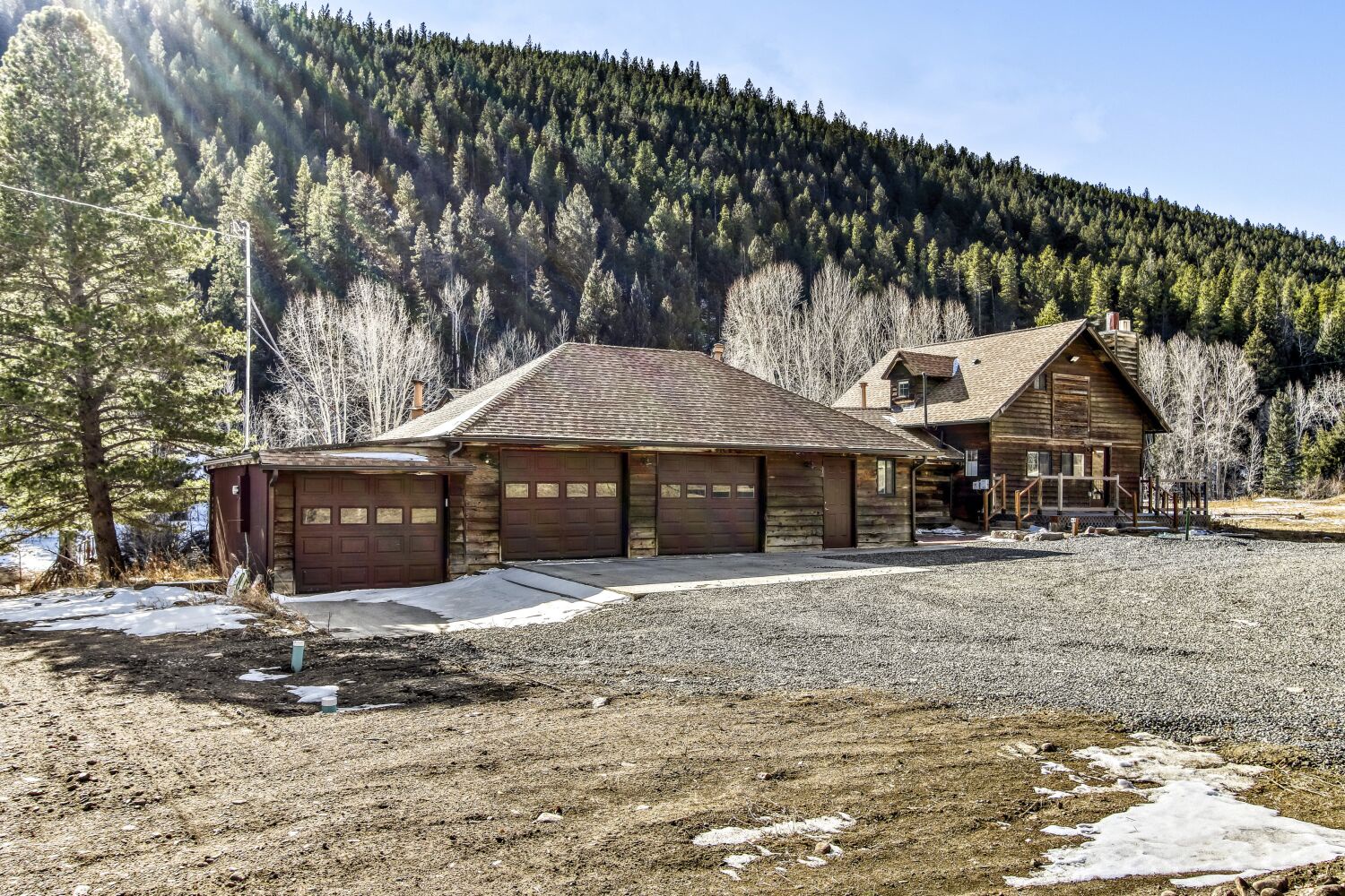 A rustic mountain property with spacious garage and driveway, nestled against forested hillsides with convenient parking space.
