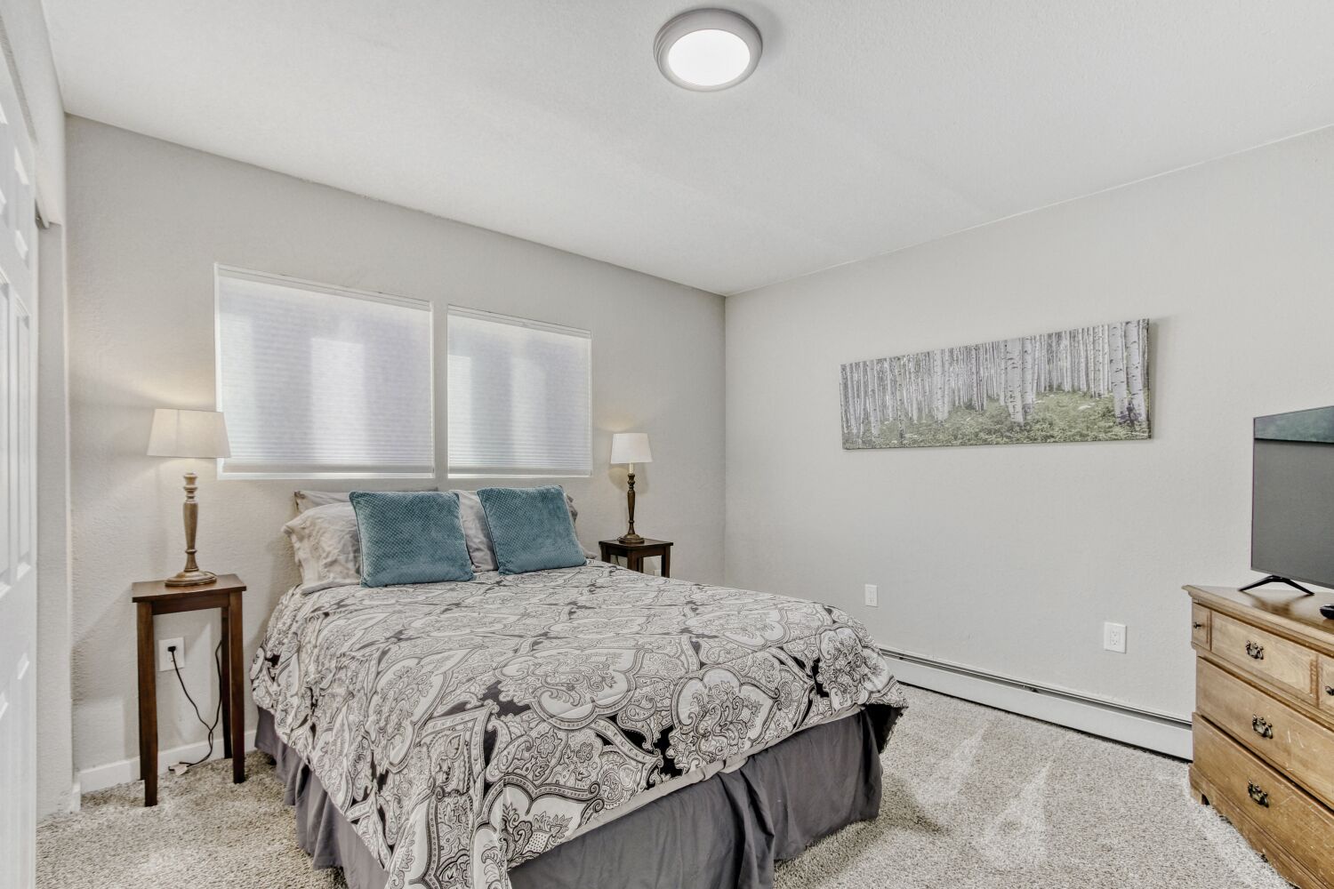 A guest bedroom with Queen size bed wrapped in elegant linens, soft natural light, and artwork that brings tranquil nature indoors.