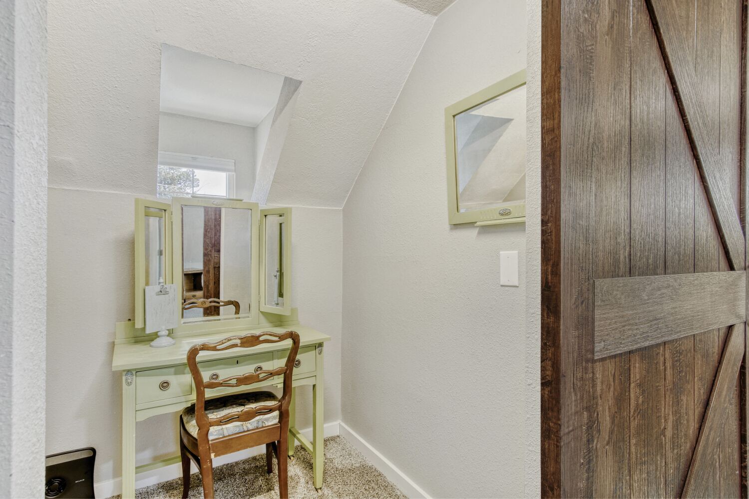 Your private vanity nook tucked behind the barn door in the primary bedroom offers a perfect spot for morning routines, featuring charming vintage-style furnishings and rustic barn door details.