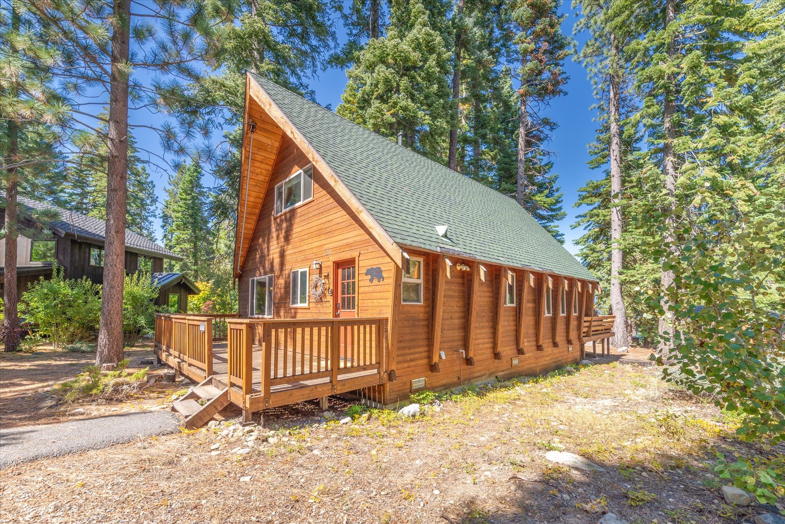 A charming A-frame cabin nestled among towering pines and surrounded by natural mountain landscape.