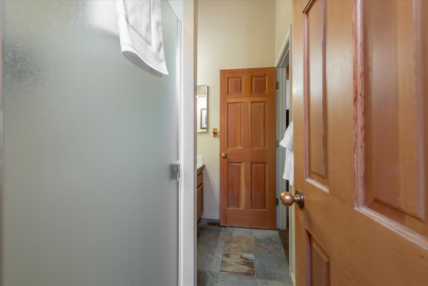 Your cozy hallway leads to private spaces, with warm wood doors, fresh towels, and charming slate floors guiding you through this inviting retreat.