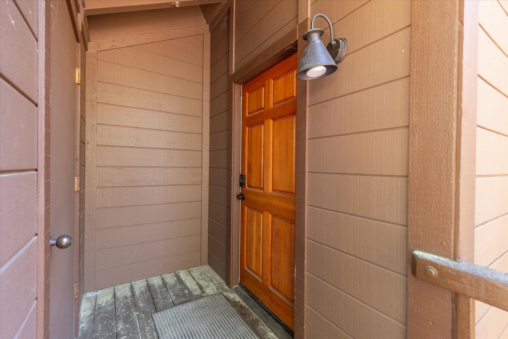 A warm wood-paneled entry frames a welcoming six-panel door, softly lit by a vintage-style sconce that sets a cozy, inviting tone from the moment you arrive.