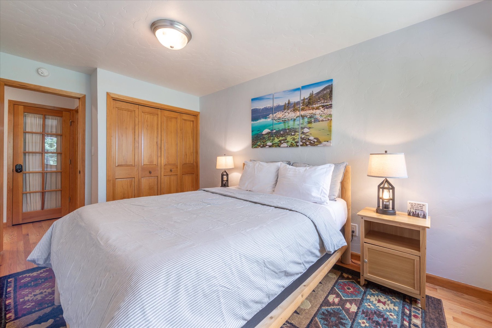 Sink into the plush king bed, where soft linens and warm lamps on either side invite your most restful night's sleep, with scenic artwork and wood accents creating a soothing retreat.