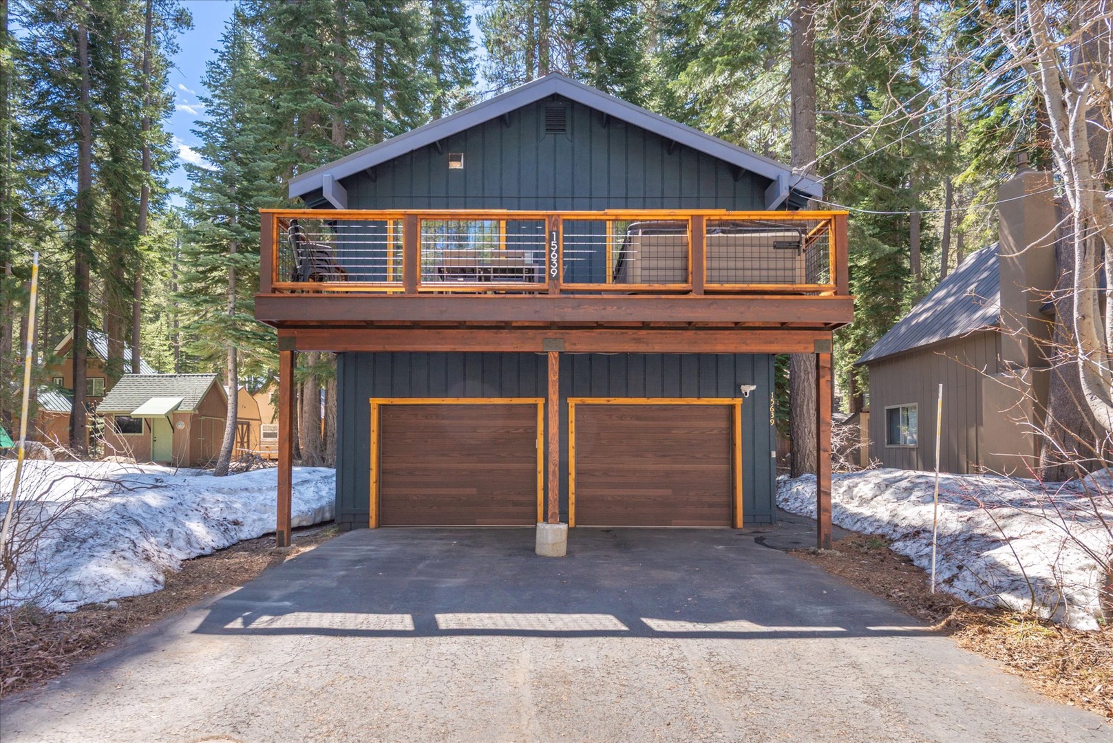 Modern mountain cabin featuring a one-car garage and spacious balcony, surrounded by towering pine trees in a peaceful forest setting.