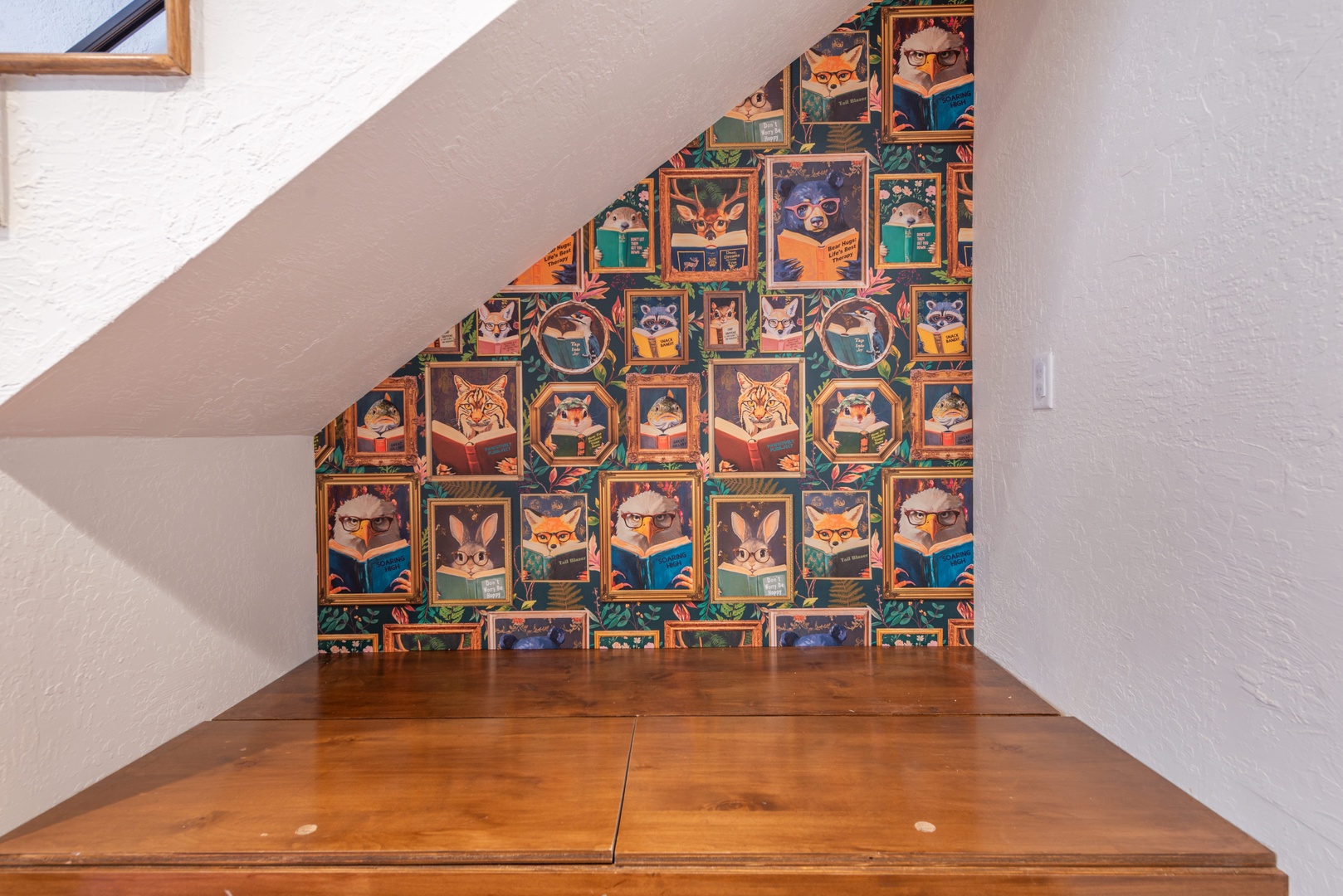 This charming reading nook under the stairs features whimsical wallpaper and warm wood flooring—your perfect hideaway for curling up with a book.