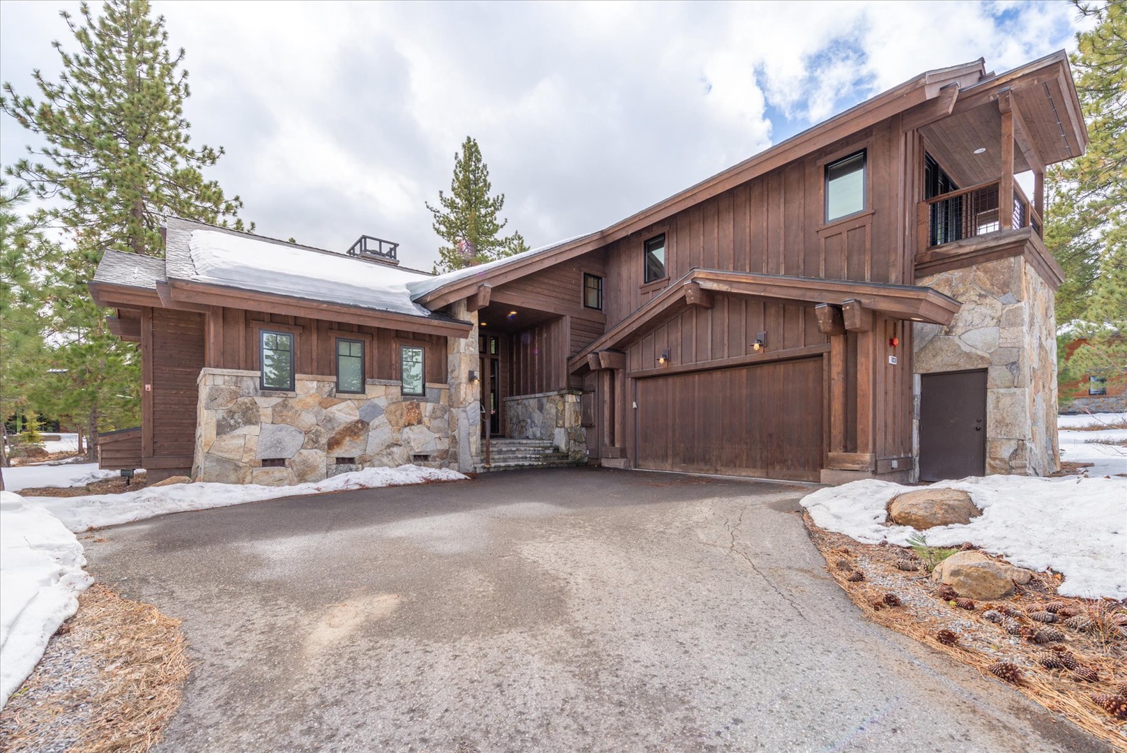 Modern mountain retreat featuring stunning wood and stone architecture with convenient driveway and garage parking.
